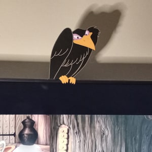 Pode incluir: Um corvo preto de desenho animado com bico e pés amarelos, empoleirado em uma superfície escura. O corvo tem uma expressão ligeiramente rabugenta, com a cabeça inclinada e os olhos semicerrados. O fundo mostra uma cena de desenho animado.