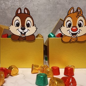 May include: Two gold boxes with lids open, each containing a small pile of green and brown wrapped candies.  A cartoon chipmunk character is peeking out of each box.