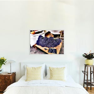 May include: A framed wall art print featuring a market scene with a large pile of dried purple lavender flowers resting on a wooden table, accompanied by a small black chalkboard sign with white handwritten text in German script.