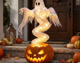 Może przedstawiać: Podświetlana dekoracja na Halloween przedstawiająca białego, półprzezroczystego ducha z tkaniny z czarnymi owalnymi oczami, unoszącego się nad wydrążoną pomarańczową dynią. Duch jest oświetlony od wewnątrz ciepłymi białymi światełkami.
