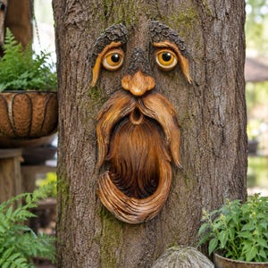 May include: A decorative tree face sculpture featuring a brown, wood-textured finish with a prominent nose, a long flowing beard, and two large, round, amber-colored eyes set beneath thick, bark-like eyebrows attached to a tree trunk.