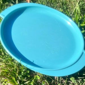 May include: A bright turquoise oval serving tray with a smooth, solid-colored surface and integrated handles on both ends. The tray features a raised rim around the perimeter, providing a defined edge for the flat, central serving area.