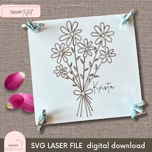 Op de afbeelding: Een lasergesneden SVG-bestand voor een gepersonaliseerd bloemenboeketontwerp. Het ontwerp bevat een boeket van eenvoudige, met lijnen getekende bloemen met een strik aan de onderkant en de naam "Krista" eronder.