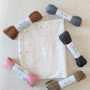 May include: A white fabric panel featuring a light gray dashed-line pattern of various dog faces, surrounded by five skeins of embroidery thread in brown, light blue, dark gray, pink, and tan, each with a white label reading Hobbyra Hobbyre.