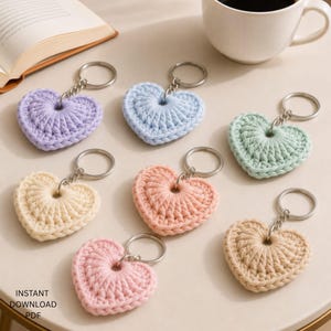 May include: A collection of seven heart-shaped keychains made from crocheted yarn in pastel colors including lavender, light blue, mint green, cream, peach, light pink, and beige, each attached to a silver-toned metal split ring.