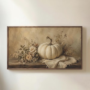 Op de afbeelding: Een rechthoekig ingelijst wandkunstwerk met een olieverfschilderij van een bleke crèmekleurige pompoen op een donkerhouten ondergrond. Naast de pompoen liggen gedroogde bloemen en een gedrapeerde, gestructureerde stof tegen een neutrale achtergrond.
