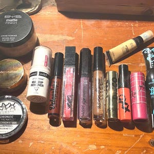 Puede incluir: Una colección de productos de maquillaje que incluye un polvo suelto mate BYS, un compacto Nude by Nature, un polvo dúo cromático NYX, una barra desmaquillante Wet n Wild, varios brillos labiales, un tubo de corrector y una máscara Essence Lash Princess.