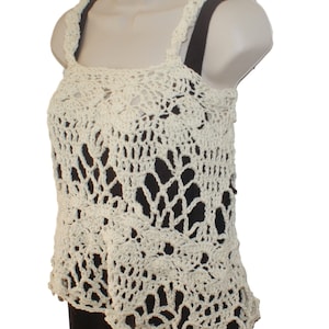 May include: A white crocheted tank top with a delicate, lacy pattern. The top has a square neckline and thin straps.