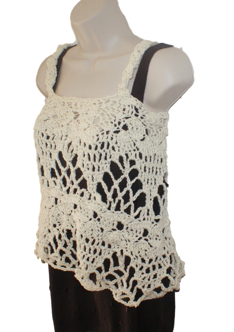 May include: A white crocheted tank top with a delicate, lacy pattern. The top has a square neckline and thin straps.