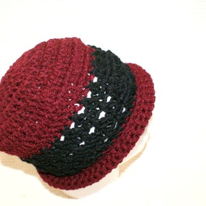May include: A crocheted hat with a burgundy and black color scheme. The hat is made with a textured stitch and has a rounded shape.