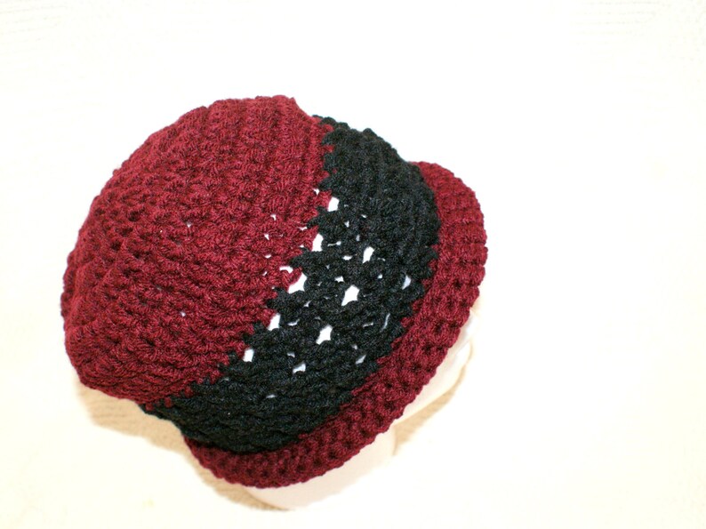 May include: A crocheted hat with a burgundy and black color scheme. The hat is made with a textured stitch and has a rounded shape.