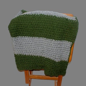 Puede incluir: Una manta de punto de crochet a rayas verdes y grises drapeada sobre una silla de madera.