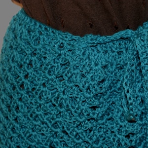 May include: Teal crochet skirt with a decorative pattern. The skirt is tied at the waist with a matching teal fabric.