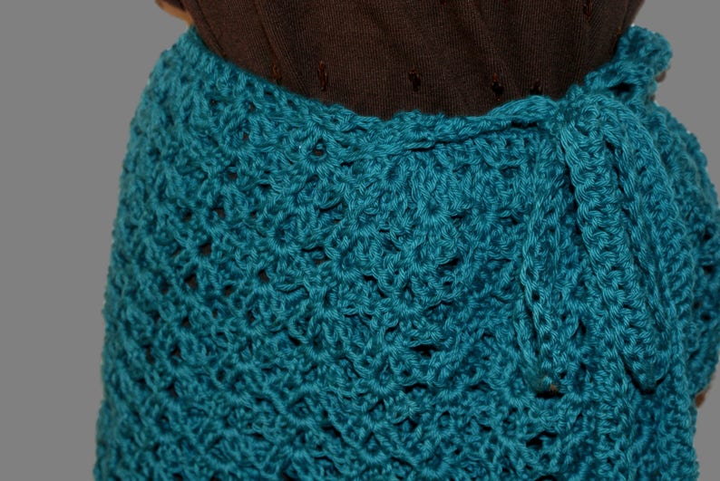 May include: Teal crochet skirt with a decorative pattern. The skirt is tied at the waist with a matching teal fabric.