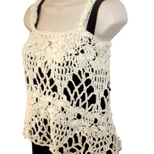 May include: A crocheted cream-colored tank top with a delicate floral pattern. The top has a loose fit and a scalloped hem.