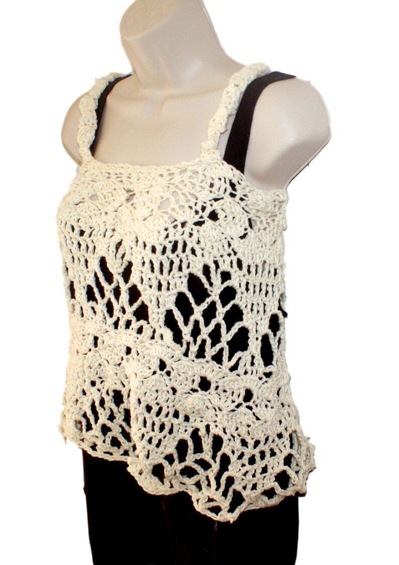May include: A crocheted cream-colored tank top with a delicate floral pattern. The top has a loose fit and a scalloped hem.