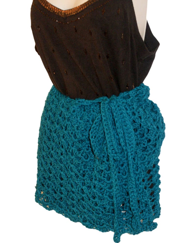 May include: Teal crochet wrap skirt with a delicate openwork pattern. The skirt is tied at the waist and falls to the mid-thigh.