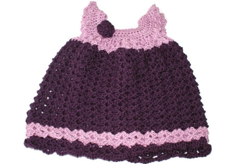 May include: A crocheted baby dress with a purple bodice and pink straps and trim.