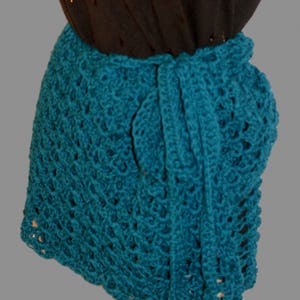 May include: Teal crochet wrap skirt with a delicate openwork pattern. The skirt is tied at the waist with a long sash.
