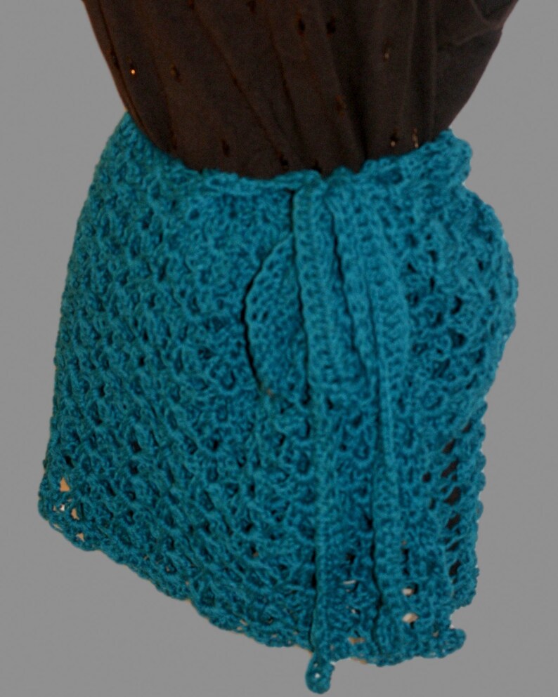 May include: Teal crochet wrap skirt with a delicate openwork pattern. The skirt is tied at the waist with a long sash.