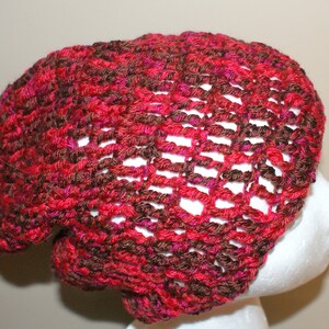 May include: A crocheted beanie hat in a red and brown color combination. The hat has a loose, slouchy fit and a lacy pattern.