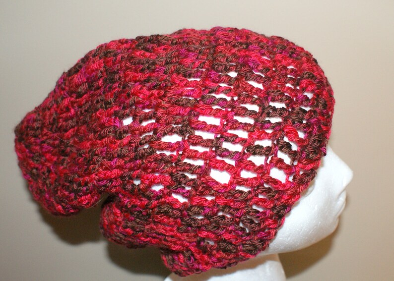 May include: A crocheted beanie hat in a red and brown color combination. The hat has a loose, slouchy fit and a lacy pattern.
