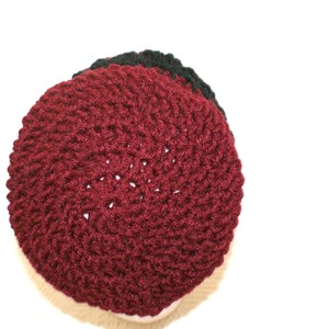 May include: A close-up of a crocheted hat with a burgundy top and a black brim.