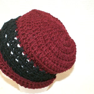 May include: A crocheted beanie hat with a burgundy top and a black band around the bottom.