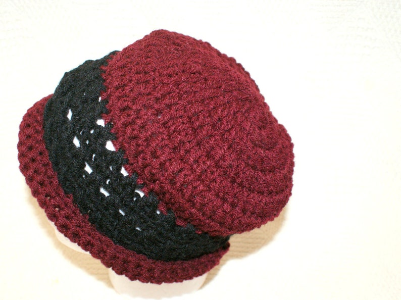 May include: A crocheted beanie hat with a burgundy top and a black band around the bottom.