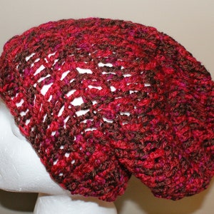 May include: A red and brown crocheted beanie hat with a loose, slouchy fit.