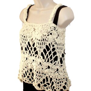 May include: A crocheted tank top with a delicate, lacy design in a cream color. The top has a square neckline and thin straps.