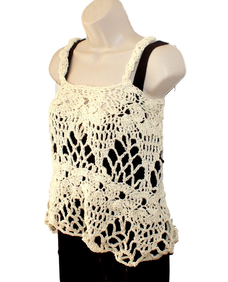 May include: A crocheted tank top with a delicate, lacy design in a cream color. The top has a square neckline and thin straps.