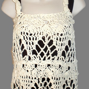 May include: A white crocheted tank top with a delicate lace pattern. The top has a scoop neck and thin straps.