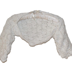 May include: A white crocheted shrug with long sleeves. The shrug is made of a delicate, open-stitch pattern.