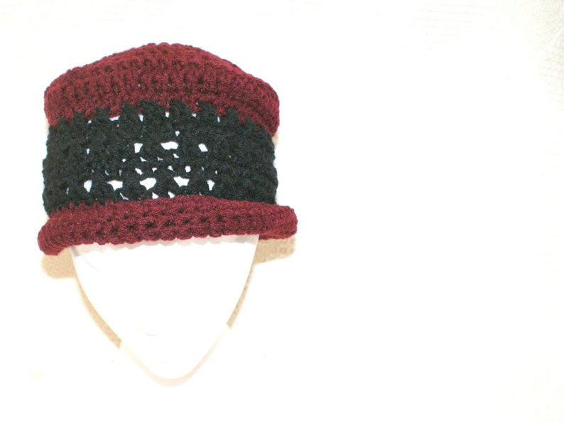 May include: A crocheted hat with a burgundy and black color scheme. The hat has a wide brim and a textured design.