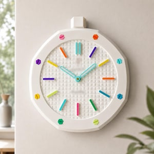 May include: A white circular wall clock with a textured grid face and a small square protrusion at the top. The clock features colorful, multi-colored hour markers and light blue hour and minute hands, creating a bright and playful aesthetic.