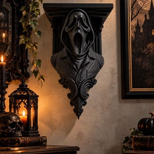 May include: A matte black wall-mounted shelf featuring a sculpted bust of a hooded figure with an elongated, open-mouthed mask. The shelf has a flat top surface and a decorative, ornate base with scrollwork details extending downward from the figure.