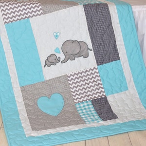May include: A turquoise and gray baby quilt with a patchwork design. The quilt features two embroidered elephants, a heart, and a chevron pattern.