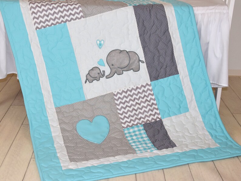 May include: A turquoise and gray baby quilt with a patchwork design. The quilt features two embroidered elephants, a heart, and a chevron pattern.