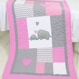 May include: Pink and gray baby quilt with a patchwork design featuring elephants, hearts, and chevron patterns.