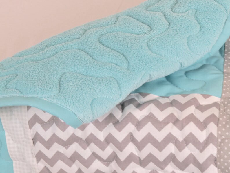 May include: A soft, blue baby blanket with a chevron pattern and a plush, textured top layer.