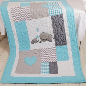 May include: A baby quilt with a patchwork design featuring gray and turquoise squares with a pattern of dots, chevrons, and gingham. The center square features two embroidered elephants with hearts.