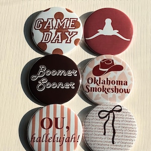 May include: Six circular pin-back buttons labeled Boomer Sooner Collection. Designs include Game Day with brown dots, a white longhorn silhouette on maroon, Boomer Sooner text, Oklahoma Smokeshow with a cowboy hat, OU, hallelujah! on stripes, and a bow.