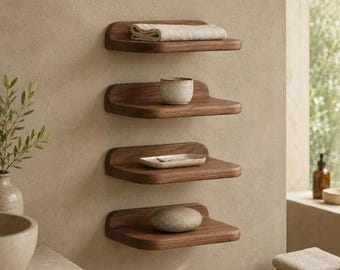 May include: Four wall-mounted wooden shelves with rounded edges. The top shelf holds a folded beige towel, the second a small ceramic bowl, the third a rectangular dish, and the bottom shelf displays a smooth, rounded stone.