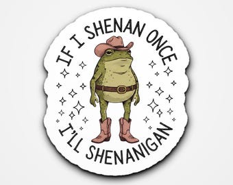 May include: A die-cut sticker featuring a green frog wearing a brown cowboy hat, a brown belt, and pink cowboy boots. The frog is surrounded by small star icons and the black text "IF I SHENAN ONCE I'LL SHENANIGAN" written in a circular pattern.
