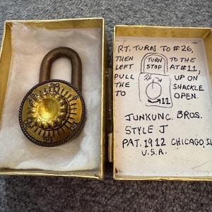May include: A vintage brass combination padlock with a circular dial featuring numbers 0 through 30, housed in a gold-coloured box. The box lid contains handwritten instructions: RT. TURN TO #26, THEN LEFT TO #11, PULL UP ON SHACKLE TO OPEN. JUNKUNC. BROS. STYLE J PAT. 1912 CHICAGO, IL U.S.A.