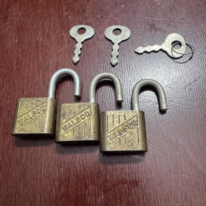 May include: Three brass-colored metal padlocks with silver-toned shackles, each featuring the embossed text WALSCO and diagonal line detailing. Three matching silver-toned metal keys are positioned above the padlocks, one attached to a small ring.