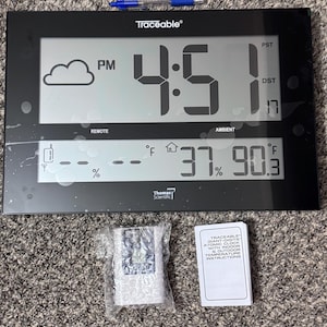 May include: A black Traceable digital atomic clock with a large display showing 4:51 PM, a cloud icon, and temperature readings of 37% humidity and 90.3 degrees Fahrenheit. Includes a blue pen, a remote sensor in bubble wrap, and an instruction manual.