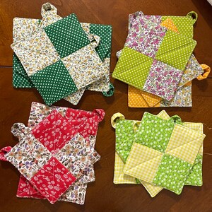 Puede incluir: Cuatro juegos de agarraderas cuadradas acolchadas con diseños de patchwork. Cada juego combina estampados florales con lunares, cuadros vichy o colores sólidos en verde, rojo, amarillo, naranja y blanco. Cada pieza incluye una pequeña presilla.