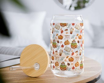 Op de afbeelding: Een doorzichtig glas met een bamboe deksel en een glazen rietje. Het glas heeft een herhalend patroon van katten in pompoenkostuums, herfstbladeren, dennenappels, boeken en koffiekopjes met de tekst Pumpkin Spice in bruine letters.